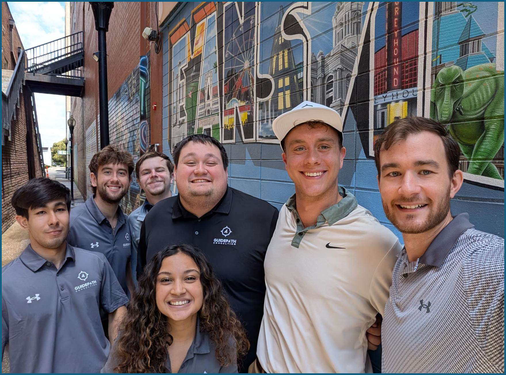 A group selfie of the Guidepath Consulting team gathered in the alley beside the Evansville mural